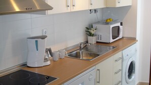 Una cocina moderna con campana de acero inoxidable, microondas integrado, cafetera, lavabo y lavadora.