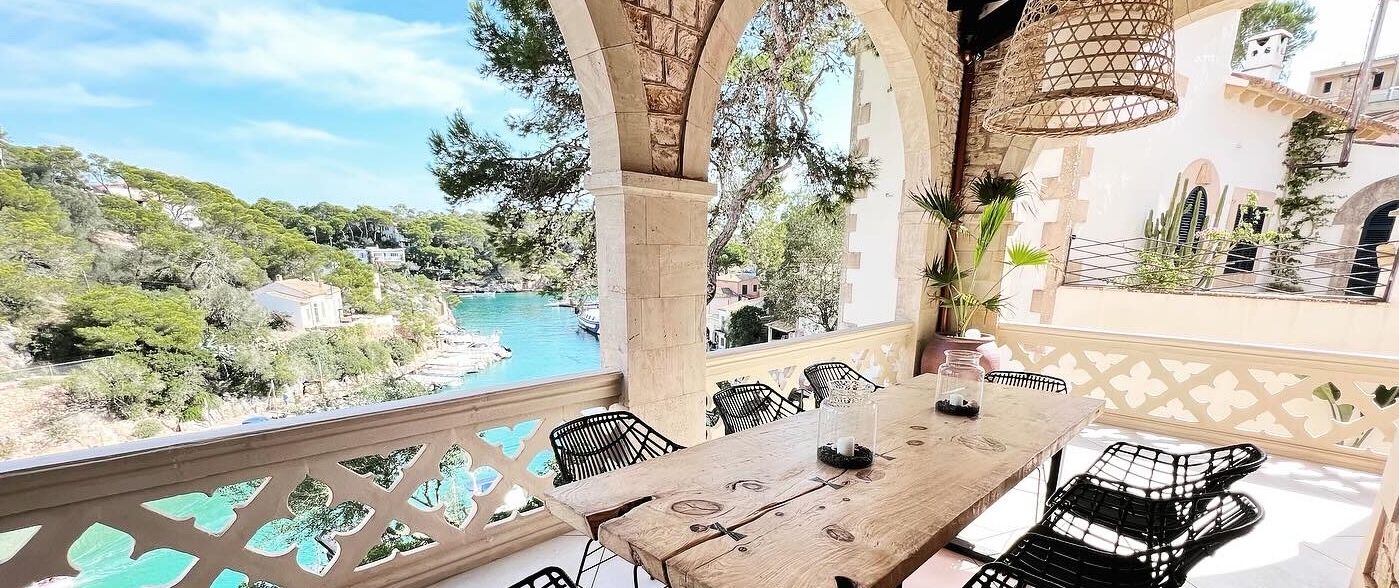 A terrace with a wooden table and chairs, overlooking a river and greenery.
