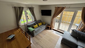 A spacious living area with a sofa, a wooden dining table, and a television mounted on the wall. - Harlyn Bay Padstow, 70 Steps from the Beautiful Stunning Beach, Parking  Garden (harlyn bay padstow)