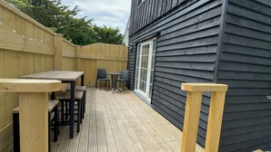 A wooden deck with a table and chairs, a window, and a wooden fence. - Harlyn Bay Padstow, 70 Steps from the Beautiful Stunning Beach, Parking  Garden (harlyn bay padstow)