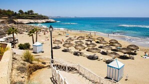 A beach with thatched umbrellas, lounge chairs, and a wooden walkway leading to the water.