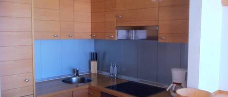 A modern kitchen with wooden cabinets, a stainless steel sink, a built-in oven, and pendant lights.