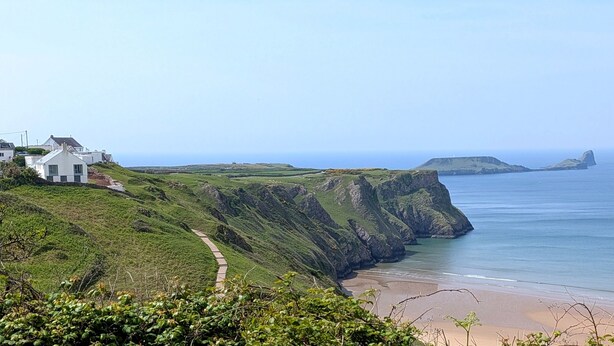 Eine Küstenlandschaft mit einem weißen Gebäude, einer Klippe und einem Strand.