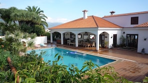 Uma área de piscina com deck revestido, espreguiçadeiras e um alpendre coberto com assentos.