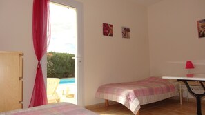 A bedroom with a bed, a desk, and a chair. There is a window with a view of a pool and greenery outside. - Superb villa with quiet pool while being close to the city center (Lorgues)