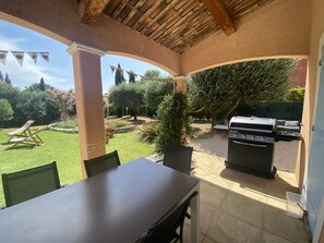 An outdoor patio with a table and chairs, a barbecue grill, and a view of a landscaped garden.