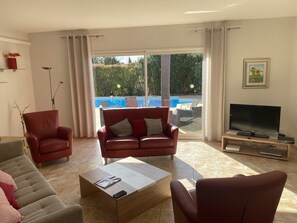 A living room with a sofa, armchairs, a coffee table, a TV, and a view of a swimming pool.