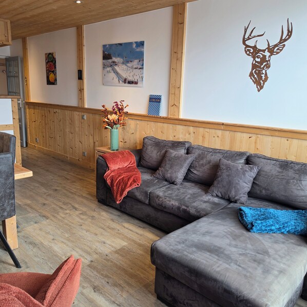 Un soggiorno moderno con un divano modulare grigio, pavimento in legno e una decorazione a testa di cervo appesa al muro.