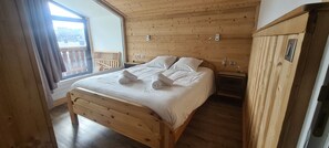 Camera da letto con rivestimento in legno, un grande letto, un comodino e vista verso il balcone esterno.