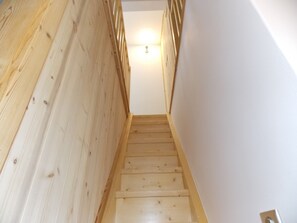 Eine Holzt Treppe mit Handlauf, die zu einem Zimmer mit weißen Wänden und einer Deckenleuchte führt.