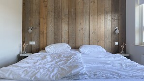 Une chambre à coucher avec une tête de lit en bois, deux tables de chevet avec des lampes et un lit recouvert de linge de lit blanc.
