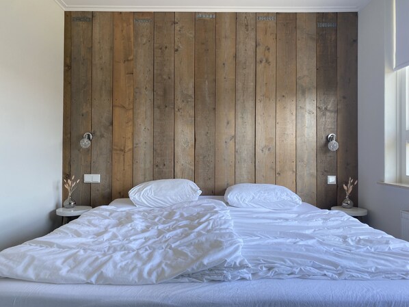 A bedroom with a wooden headboard, two bedside tables with lamps, and a bed with white bedding.