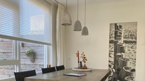 Un espace repas avec une grande table en bois, des chaises noires et des luminaires suspendus.