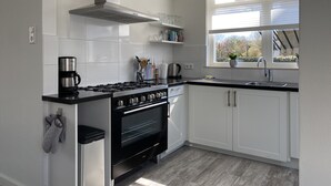 Une cuisine moderne avec des meubles blancs, une cuisinière en acier inoxydable et une fenêtre donnant sur les arbres.