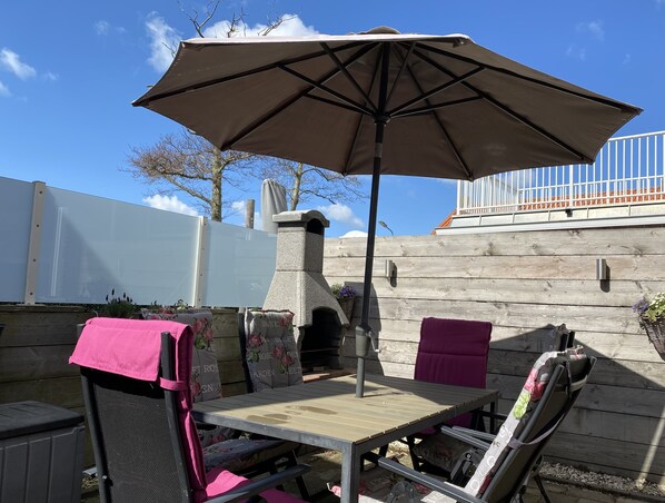 An outdoor patio with a table and chairs, a stone chimney, and a large umbrella. - Property next to the mill of Westkapelle! (Westkapelle)