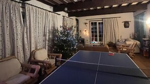 A room with a ping pong table, a Christmas tree, and a cozy seating area with chairs and a sofa. - 🌸 La Maison Rose – Your Dream French Countryside Escape 🌸 (Marsac)