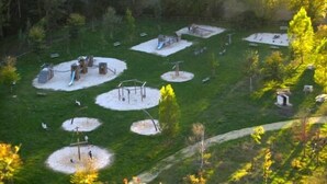 Un parc doté de diverses installations de jeux et d’espaces verts ouverts, le tout entouré d’arbres.