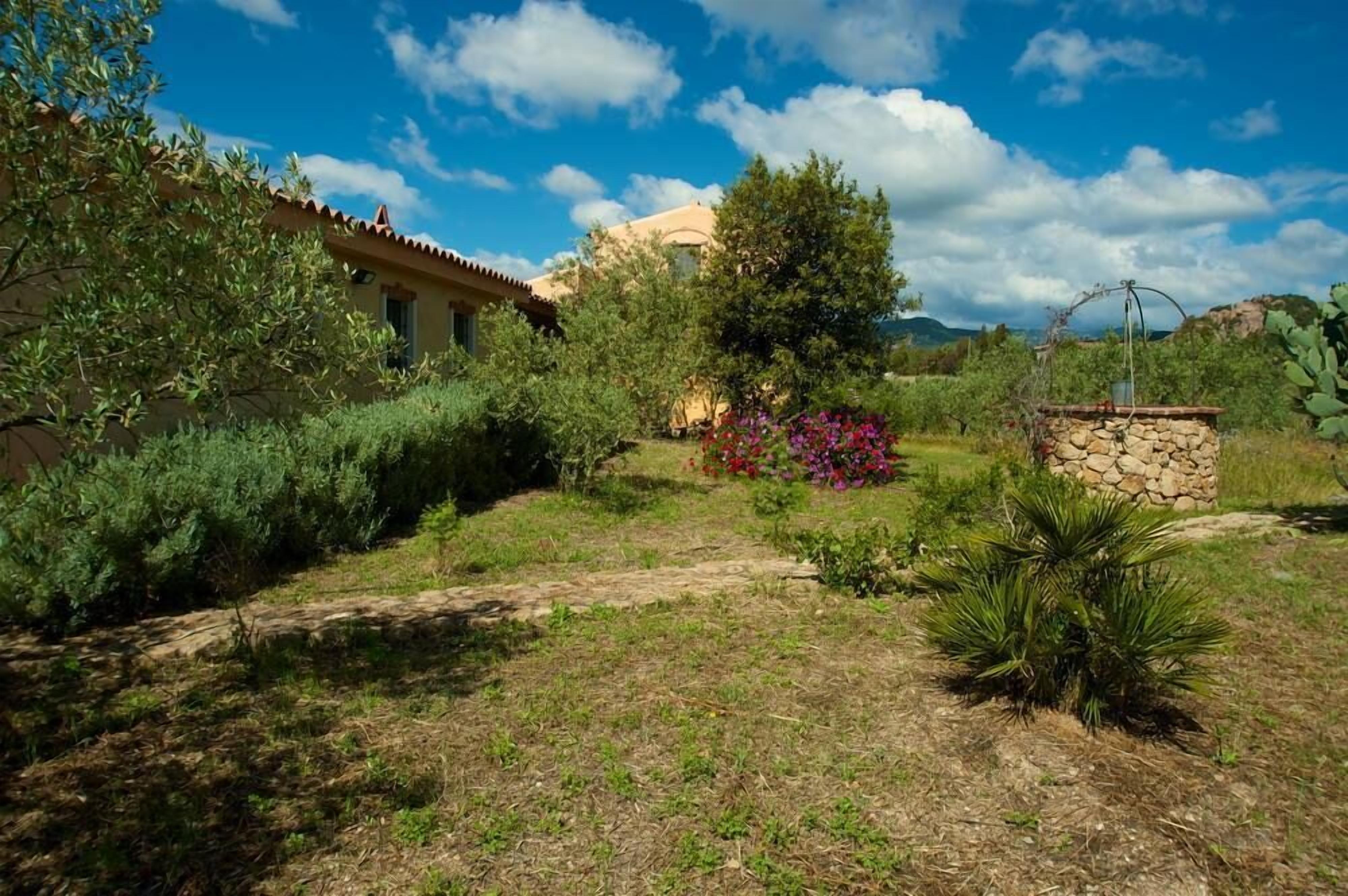 A rustic house with a stone wall and a garden with various plants and flowers.