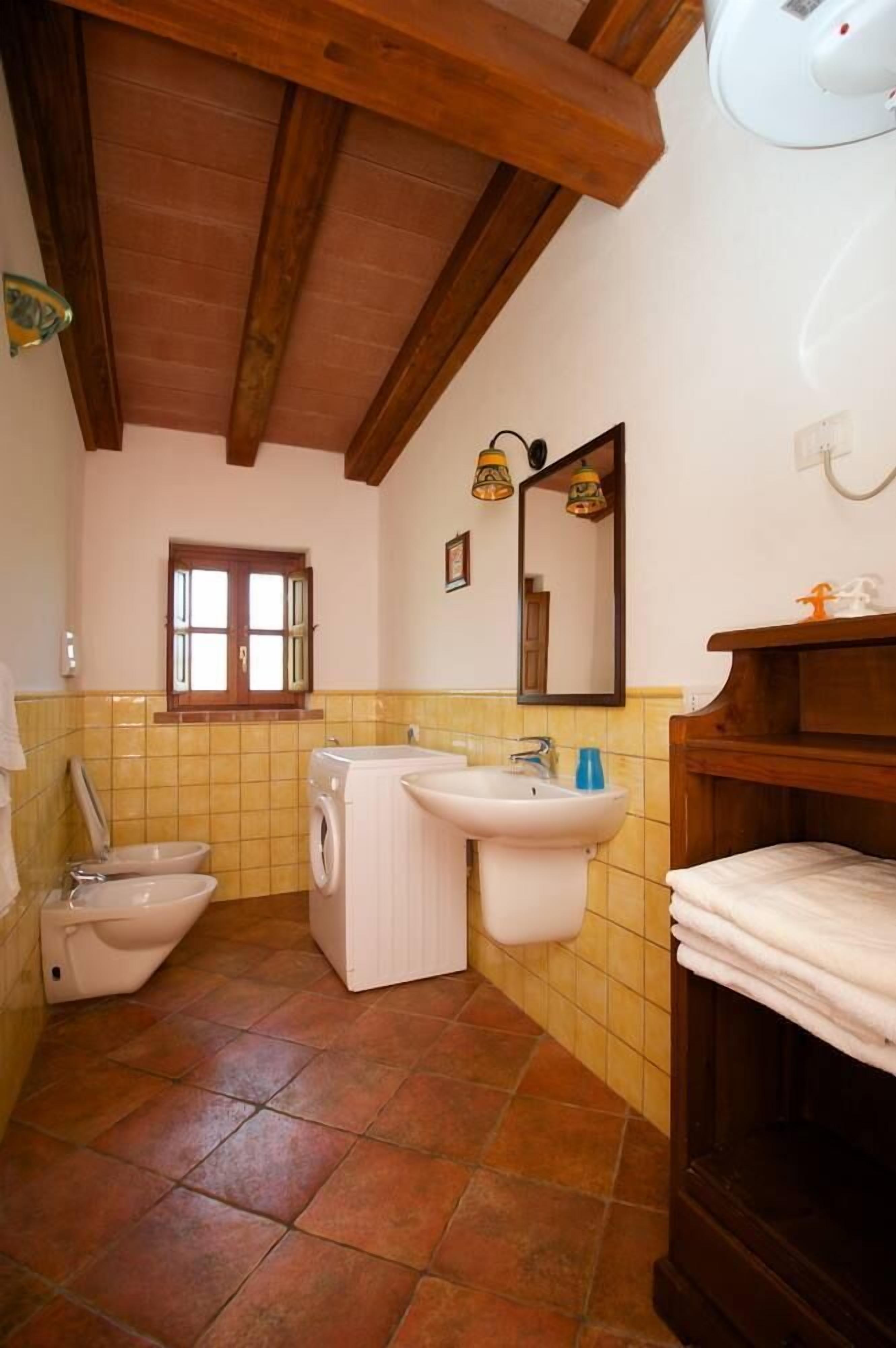 Ein kleines Badezimmer mit Waschmaschine, zwei Waschbecken, Toilette und Holzboden.