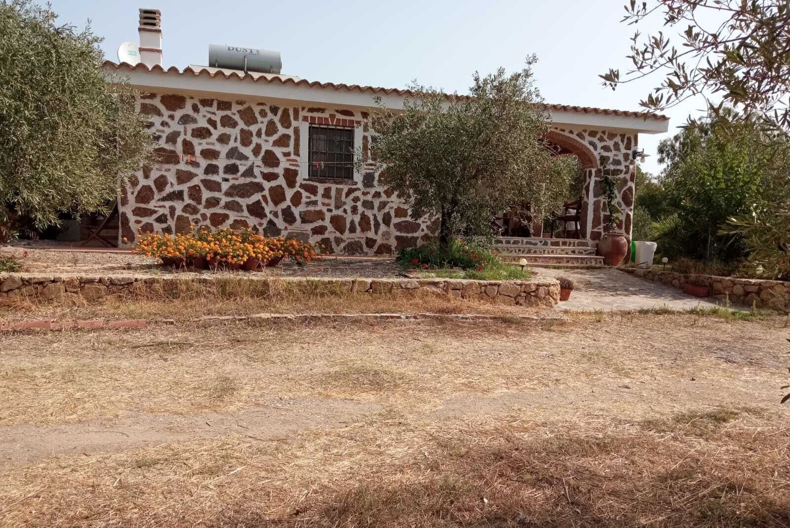Il s’agit d’un bâtiment en pierre, doté d’un toit en tuiles, d’une petite fenêtre et d’une porte. Un jardin s’y trouve, avec de l’herbe sèche et quelques plantes en pot.