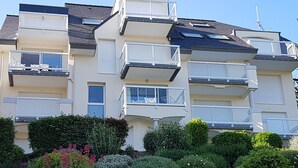 A multi-story residential building with balconies, a flat roof, and a garden area with various plants and flowers. - Residential flat- ST-CAST-LE-GUILDO (Saint-Cast-le-Guildo)