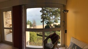 A room with a large bay window overlooking a beach and greenery. - Residential flat- ST-CAST-LE-GUILDO (Saint-Cast-le-Guildo)