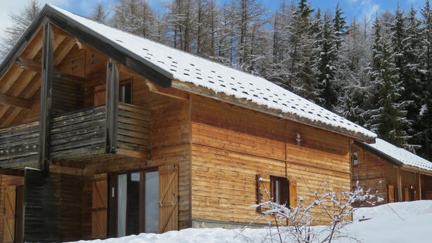 Une cabane en bois avec un toit enneigé, de grandes fenêtres et un balcon.