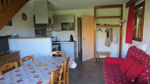 Un espace de vie compact comprenant un coin repas, une kitchenette et un canapé rouge.