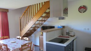 Une cuisine avec un escalier en bois, une table avec des chaises et une horloge au mur.