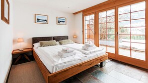 A bedroom with a wooden bed, two bedside lamps, a large window with a view, and two framed pictures on the wall. - Uninterrupted Eiger Views, 150m from Cable Car (Grindelwald)