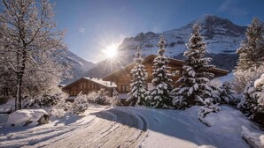 A wooden lodge with a ski slope in the foreground, surrounded by snow-covered trees and mountains. - Uninterrupted Eiger Views, 150m from Cable Car (Grindelwald)