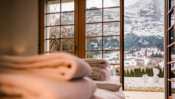 A room with a large window offering a view of a snowy mountain landscape. - Uninterrupted Eiger Views, 150m from Cable Car (Grindelwald)