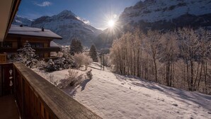 A snow-covered mountain landscape with a wooden cabin and a clear view of the sun shining through the trees. - Uninterrupted Eiger Views, 150m from Cable Car (Grindelwald)