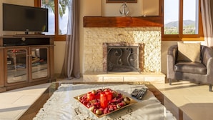 Una sala de estar con televisión, chimenea, sofá y una mesa con candelabros y frutas.