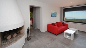 Un salon moderne avec une cheminée, un canapé rouge et une grande fenêtre donnant sur l’extérieur.