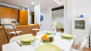 A dining area with a table set for four, featuring green plates, cutlery, and glasses. There are chairs around the table, and a kitchen area is visible in the background. - 3 bedroom apartment with sunny terrace perfect for families (Costa Adeje)