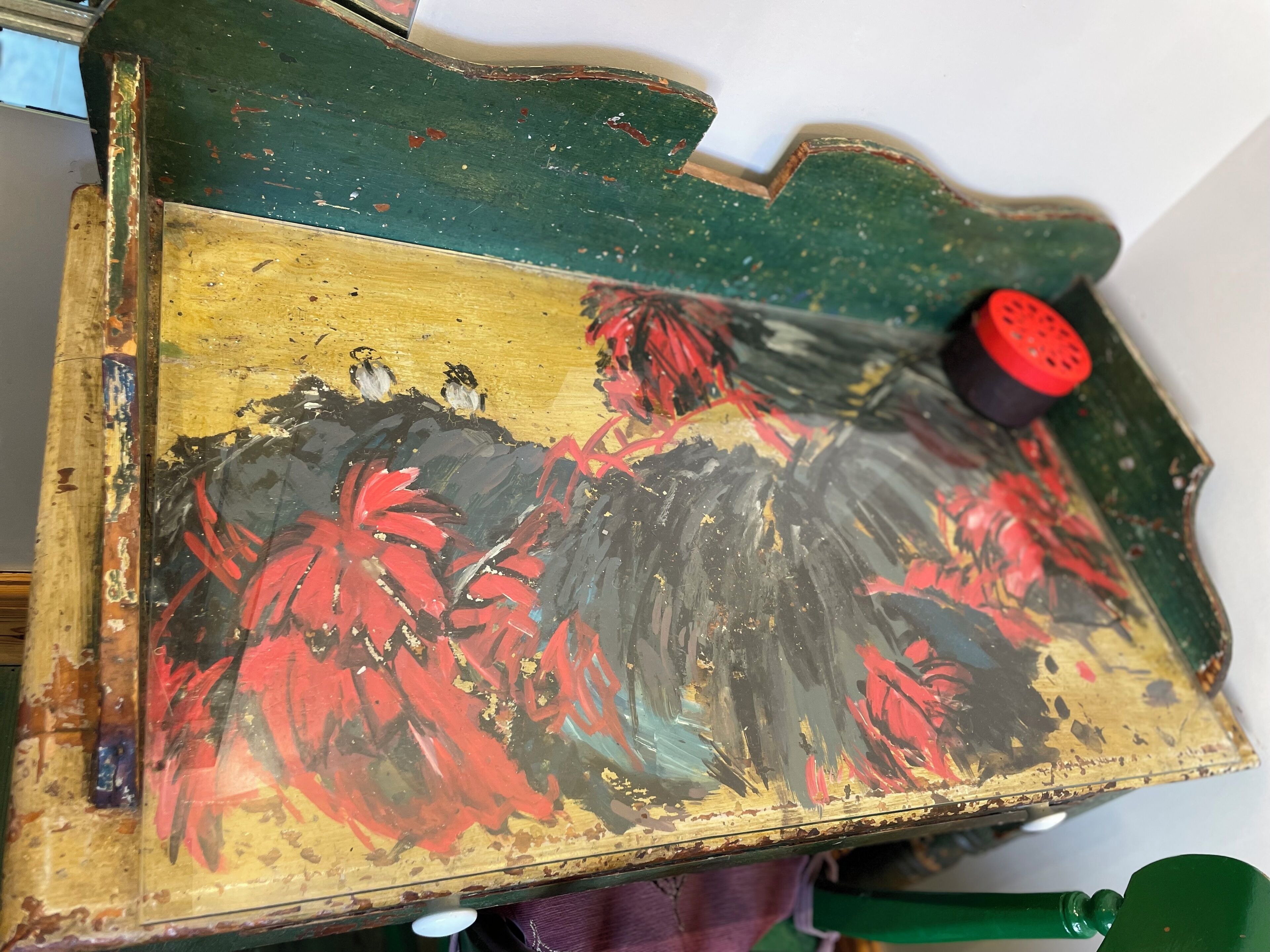 A close-up of a worn, colorful painting on a piece of furniture with a green and yellow background.