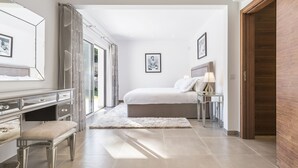 A modern bedroom with a large bed, bedside table, and a mirror. - Your private getaway in Vale do Lobo (Vale do Lobo)