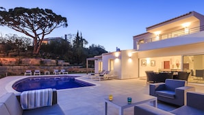 A modern outdoor pool area with a curved pool, lounge chairs, and a dining area with outdoor furniture. - Your private getaway in Vale do Lobo (Vale do Lobo)