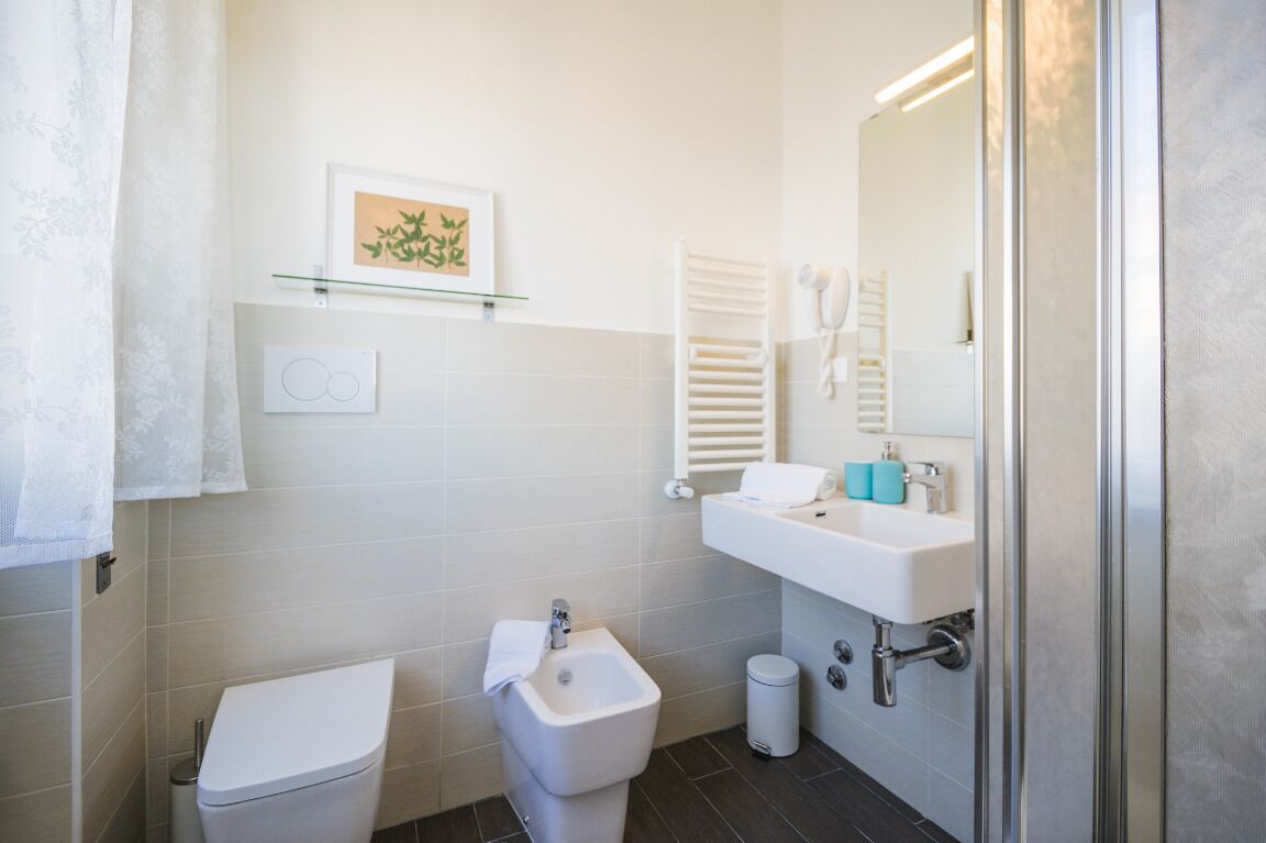 A modern bathroom with a toilet, bidet, sink, and a glass shelf with a framed picture.