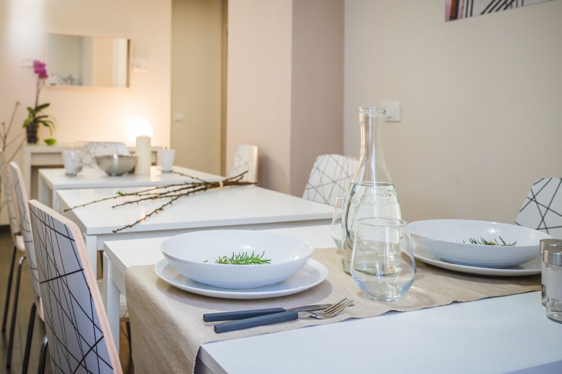 A dining table set with white plates, a clear glass pitcher, and a bowl with greenery.