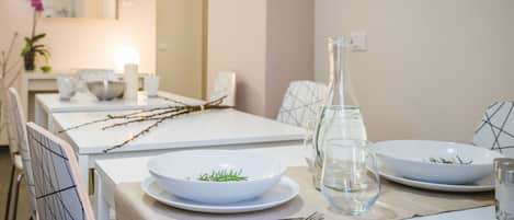 A dining table set with white plates, a clear glass pitcher, and a bowl with greenery.