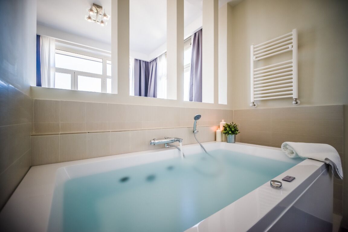 A modern bathroom with a bathtub, a towel rack, and a small plant on the counter.