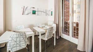 A dining area with white tables and chairs, a decorative wall piece, and a sliding glass door with a metal gate.