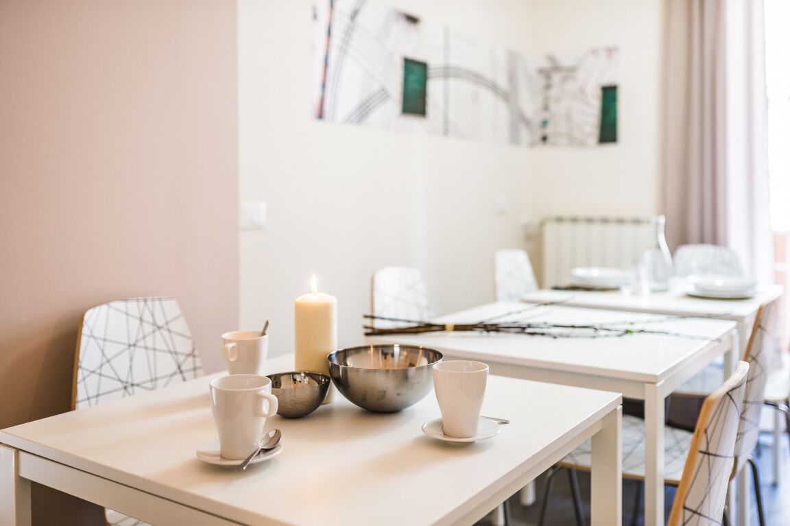 A dining area with a table set for two, featuring a candle, a metal bowl, and two cups.