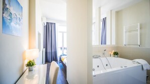 A hotel room with a bed, a bathroom with a bathtub, and a window with curtains.