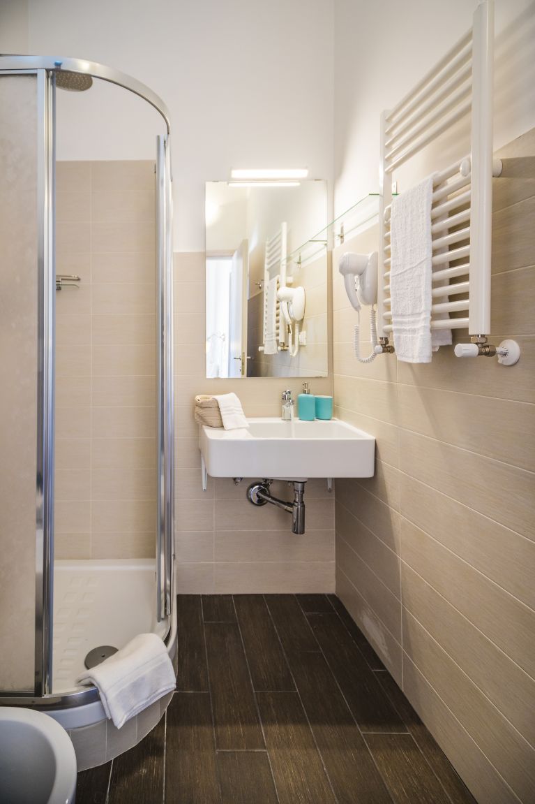 Ein modernes Badezimmer mit einer gläsernen Duschkabine, einem weißen Waschbecken mit Spiegel darüber und einem Handtuchhalter an der Wand.