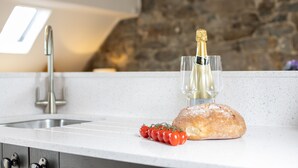 Una encimera de cocina con una hogaza de pan, una botella de champán y un racimo de tomates.