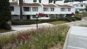 A row of white modern apartment buildings with balconies, surrounded by well-maintained gardens and hedges.