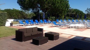 A poolside area with lounge chairs and a sofa, surrounded by trees.